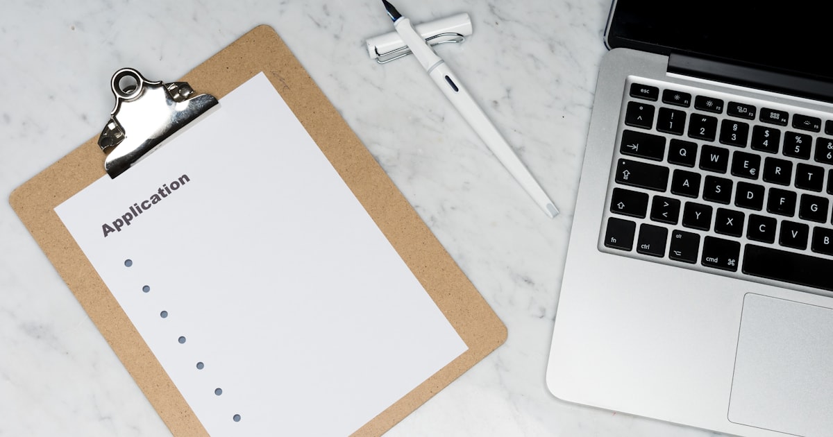 Application form on a clipboard next to a laptop